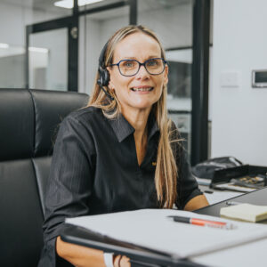 woman with phone headset sitting at a desk smiling at camera