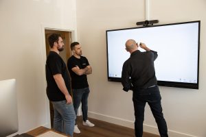 3 men standing and interacting with an interactive screen in a meeting room
